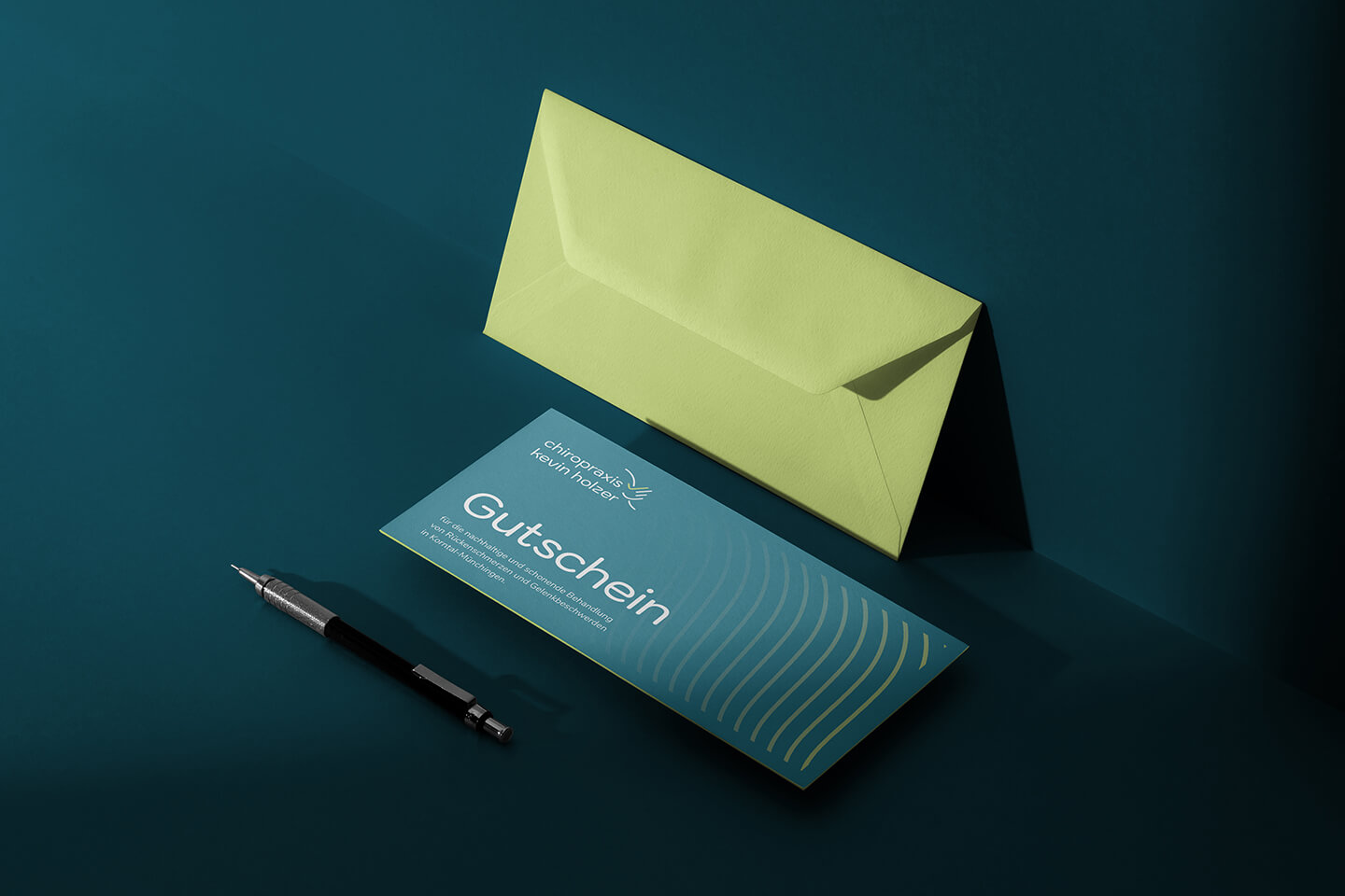 Gutschein und grüner Umschlag der Chiropraxis Kevin Holzer mit Bleistift auf hellem Untergrund.