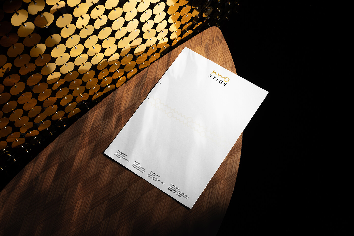 IMMOstige Briefpapier auf einem Holztisch mit goldenen runden Interieur-Details im Hintergrund.