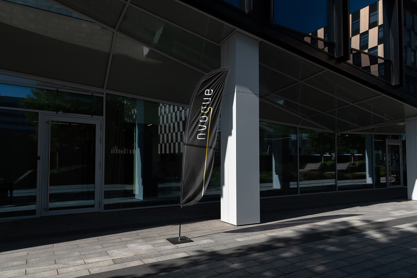 Schwarze nvogue Flagge vor einem Glasgebäude als räumliche Markenpräsenz im Außenbereich.