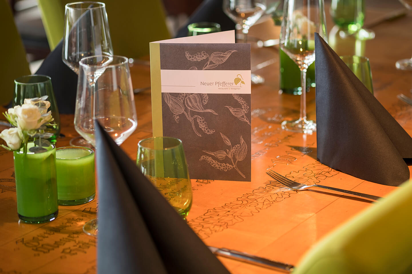 Gedeckter Tisch im Restaurant Neuer Pfefferer mit Menükarte, Gläsern, Servietten und grünen Kerzen.