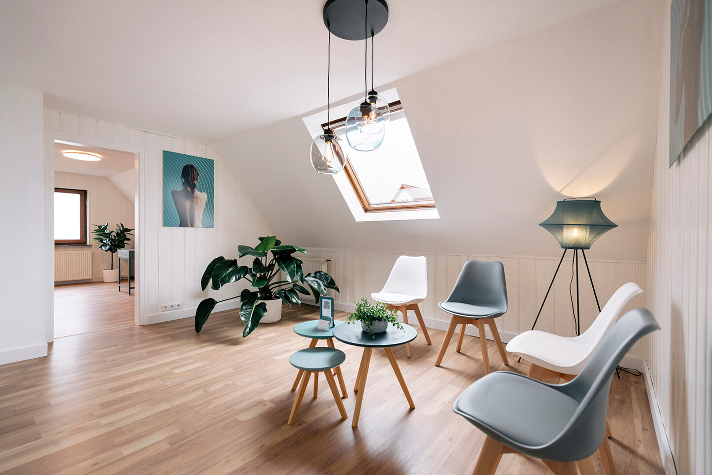 Wartebereich der Chiropraxis Kevin Holzer mit Stühlen, Pflanzen, Pendelleuchten und Wandmotiv.