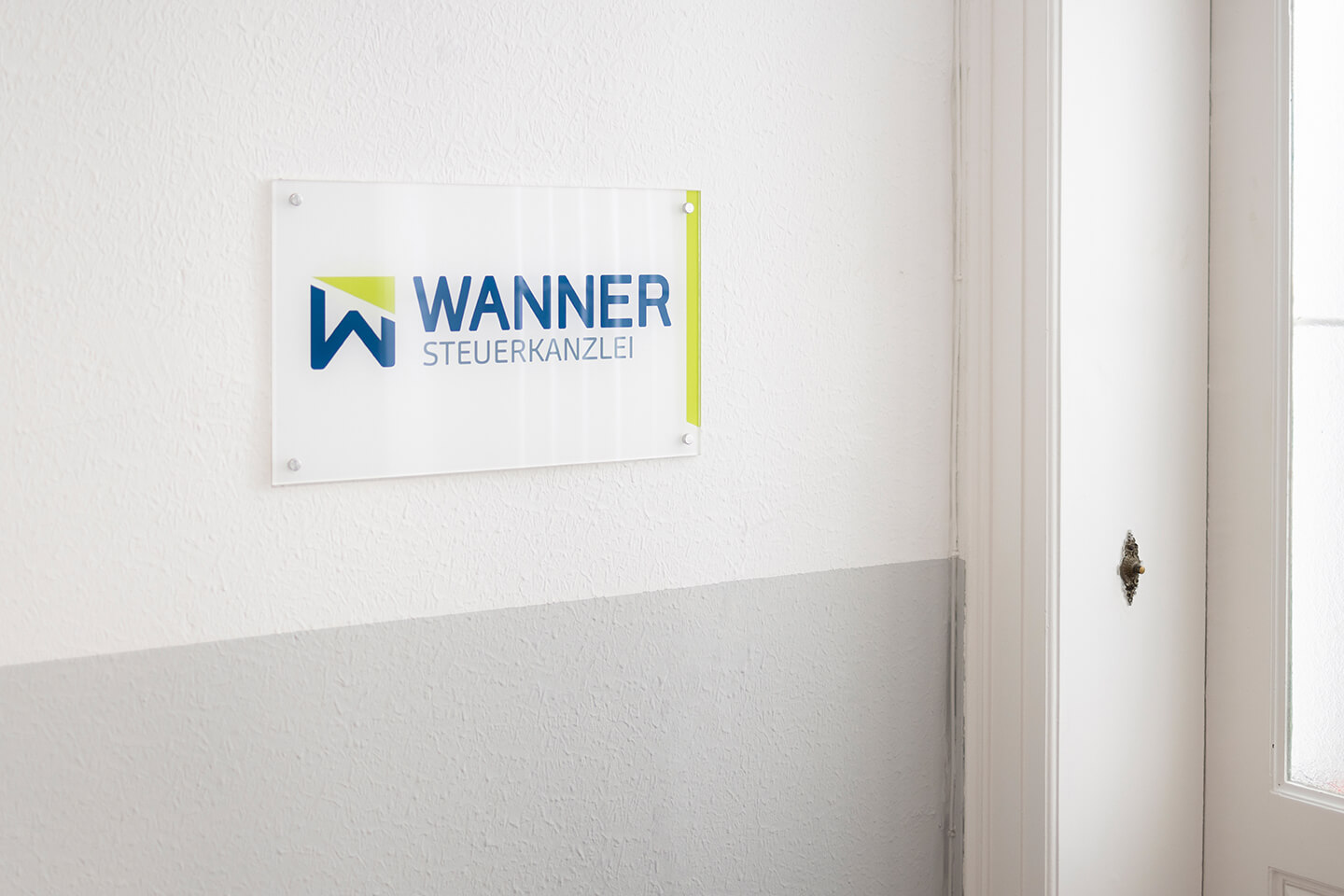 Wandschild der Steuerkanzlei Wanner in einem hellen Flur neben einer Tür.